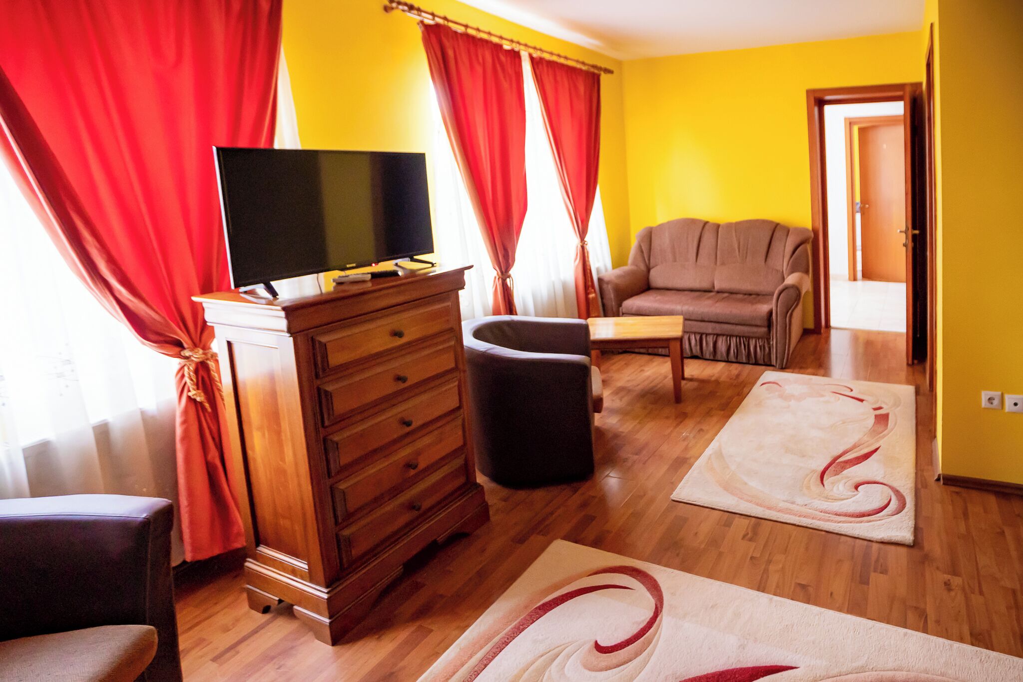 A living room with a television on a wooden cabinet, a sofa, a chair, and a rug.