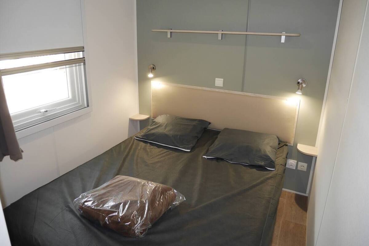 A small, single-bed room with a window, bedside lamps, and a wall-mounted shelf.