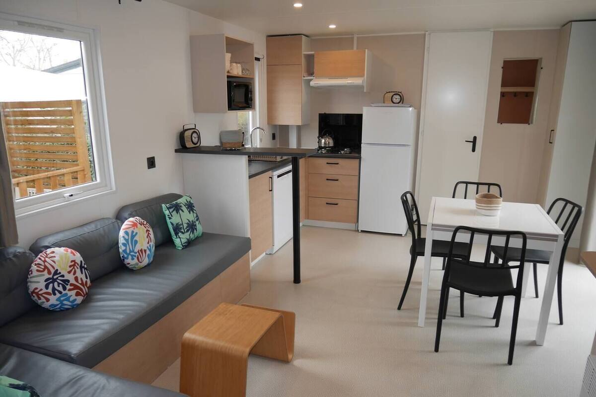 A modern kitchen with a dining area, a sofa with colorful cushions, and a small wooden stool.