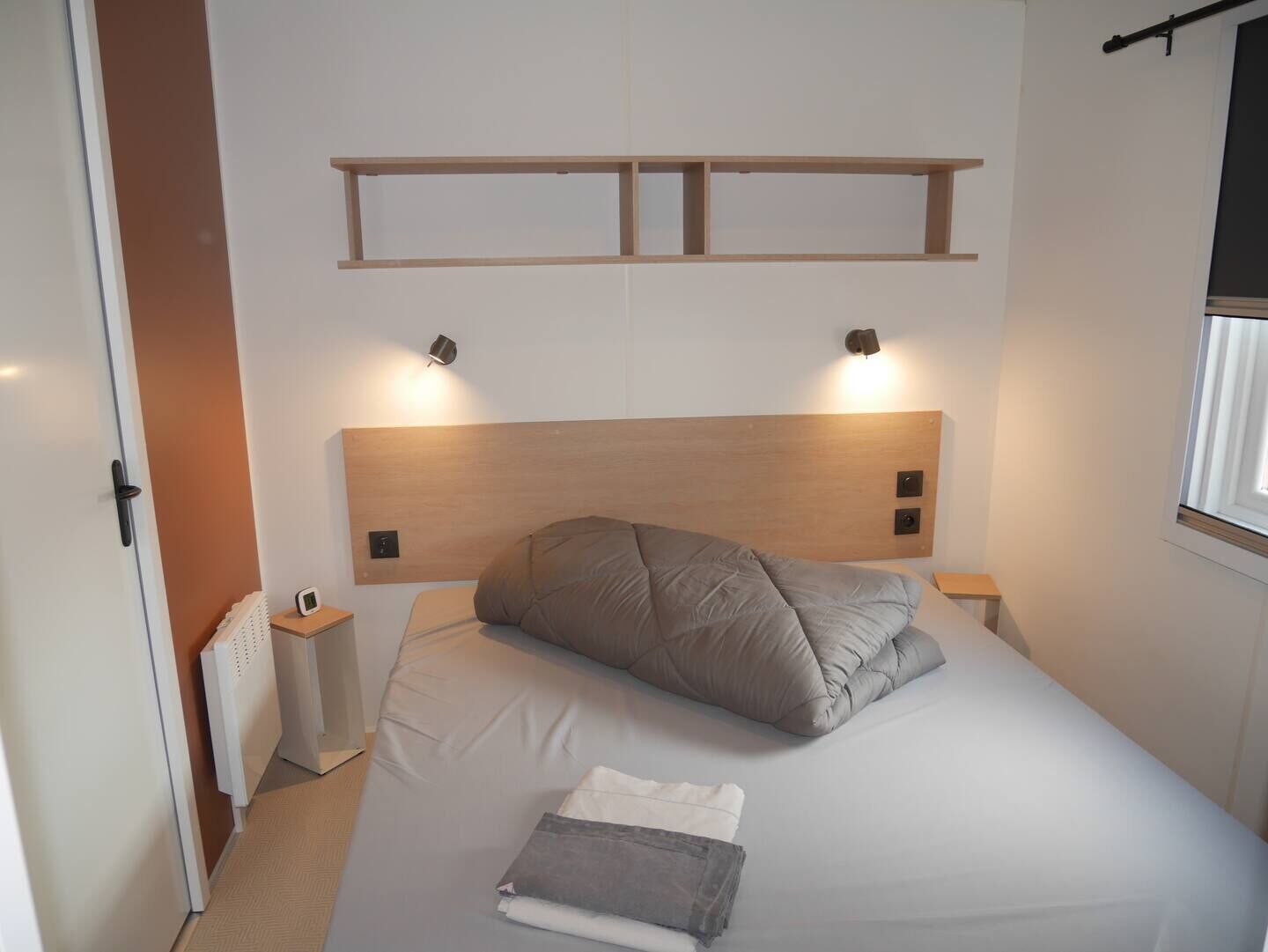A bedroom with a bed, bedside lamps, a radiator, and a window.