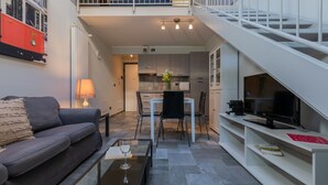 A compact living space with a sofa, a dining table with chairs, a kitchen area, and a TV on a stand. - Loft Tramvai by Wonderful Italy (Turin)