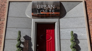 A building facade with a sign reading "URBAN LOFTS" above a red door, flanked by two green plants. - Loft Tramvai by Wonderful Italy (Turin)