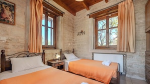 Ein Zimmer mit zwei Betten, Holz-Kopfteilen, Steinwänden und großen Fenstern mit Vorhängen.