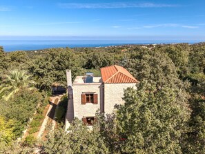 Une maison en pierre avec un toit recouvert de tuiles rouges, entourée d’une végétation luxuriante et offrant une vue sur un paysage côtier.