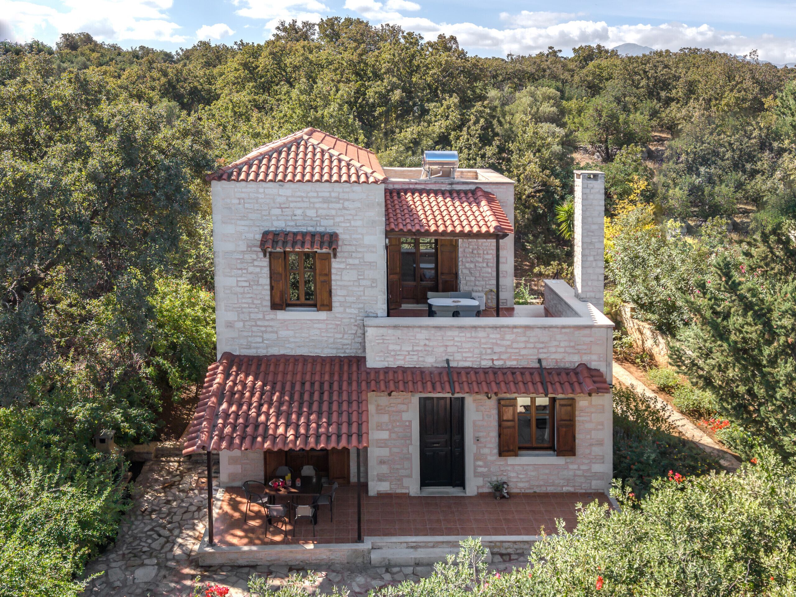 A two-story stone house with a red-tiled roof, a chimney, and a patio with outdoor furniture.