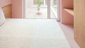 A bedroom with a sloped ceiling, a bed with a white and speckled bedspread, a wooden headboard, and a view through a glass door to an outdoor area with a plant. - Award-Winning, Magazine-Featured, Architect-Designed Lakeside Home (Vitnyéd)