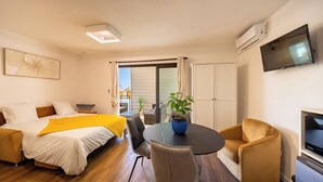 Ett modernt hotellrum med en säng, en soffa, ett matbord med stolar, en TV och en luftkonditioneringsanläggning.