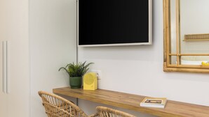 Ett modernt rum med ett skrivbord i trä, två fåtöljer i rotting, en platt-TV, en spegel och en krukväxt.