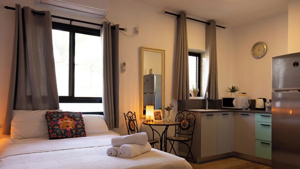 A hotel room with a bed, a small table, a chair, a microwave, a refrigerator, and a clock on the wall. - LOUI TALPIOT HOTEL: Authentic Experience. Art, Market,Rooftop & Boutique Comfort (Haifa)
