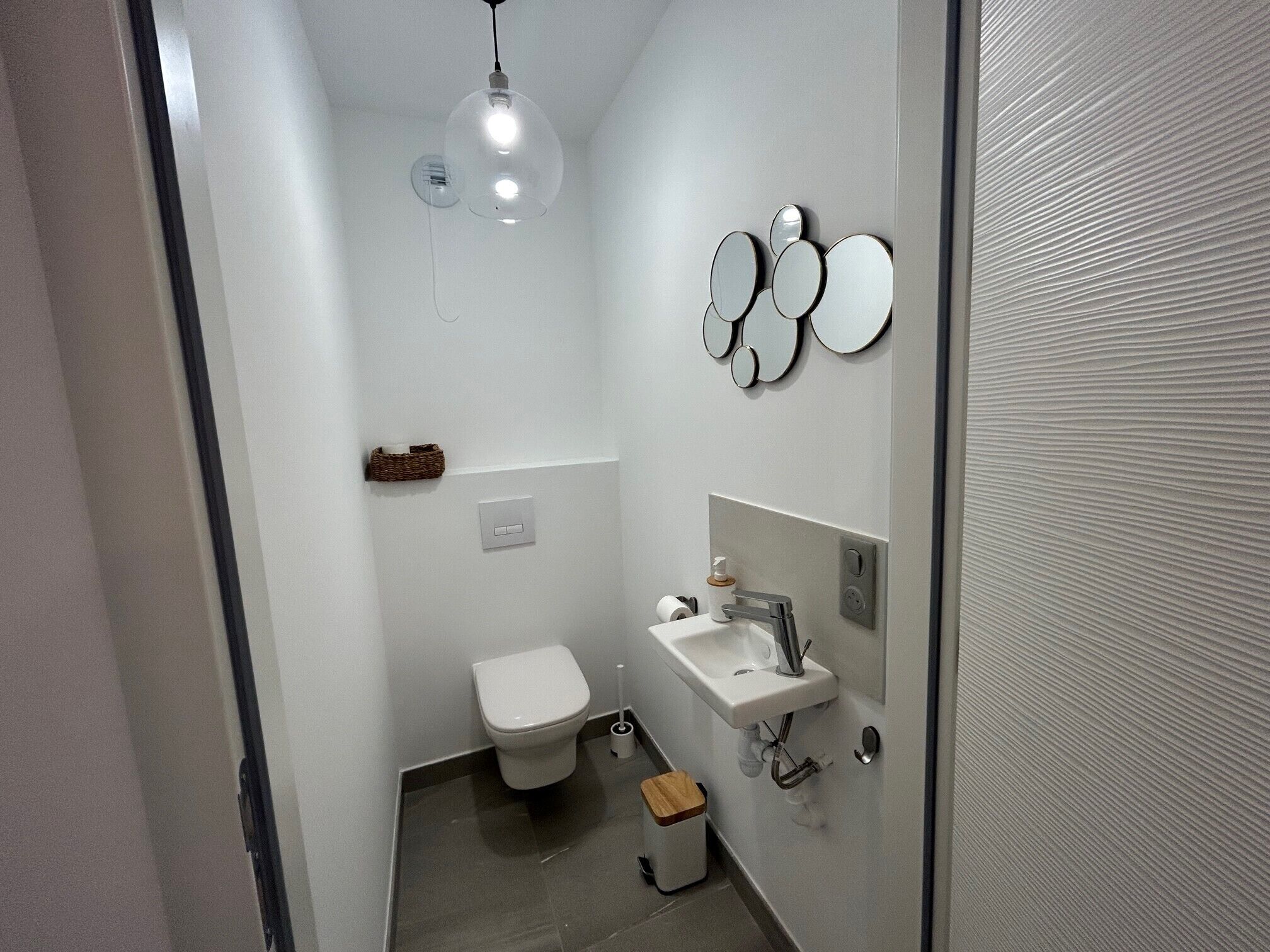 A small, modern bathroom with a toilet, sink, and a hanging light fixture.