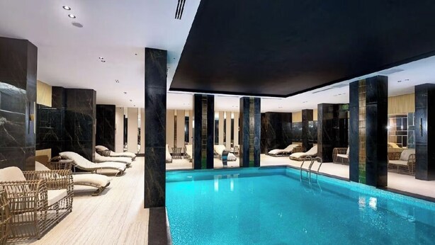 A modern indoor swimming pool with lounge chairs and a wooden floor. - Apartment 1+1 Qoople Legend B28 100 m from the sea (Alanya)