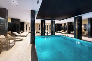 Une piscine intérieure moderne, dotée de chaises longues et d’un plancher en bois.