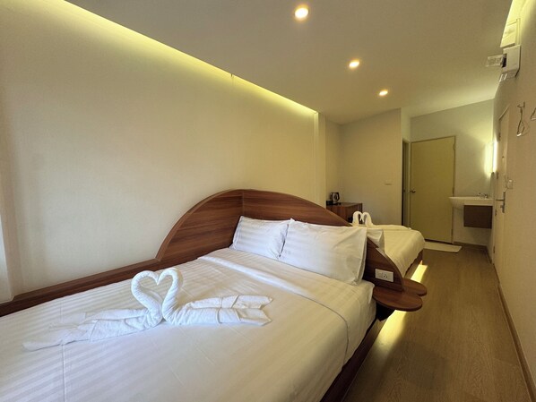 A hotel room with two beds, a wooden headboard, a heart-shaped towel arrangement, a bedside table, and a small bathroom with a sink and mirror. - Sonata siam-ratchathewi (Bangkok)