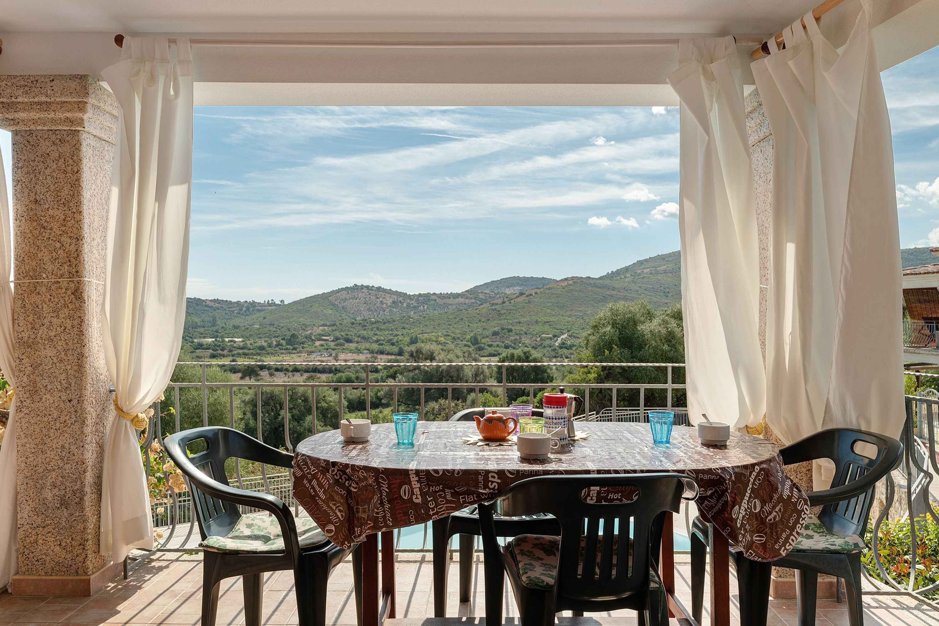 Une table dressée pour deux personnes, avec des chaises, une vue sur des collines verdoyantes et un ciel dégagé.