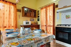 A dining area with a table set for four, a microwave, a stove, and a cabinet above the counter. - Holiday Home 'Trilocale Luana' with Sea View, Shared Pool and Air Conditioning (Maiorca)