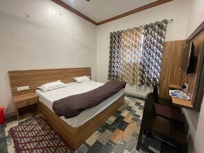 A bedroom with a wooden bed, a desk, a chair, a television, and patterned curtains. - Shree Mahidev Palace (Ayodhya)