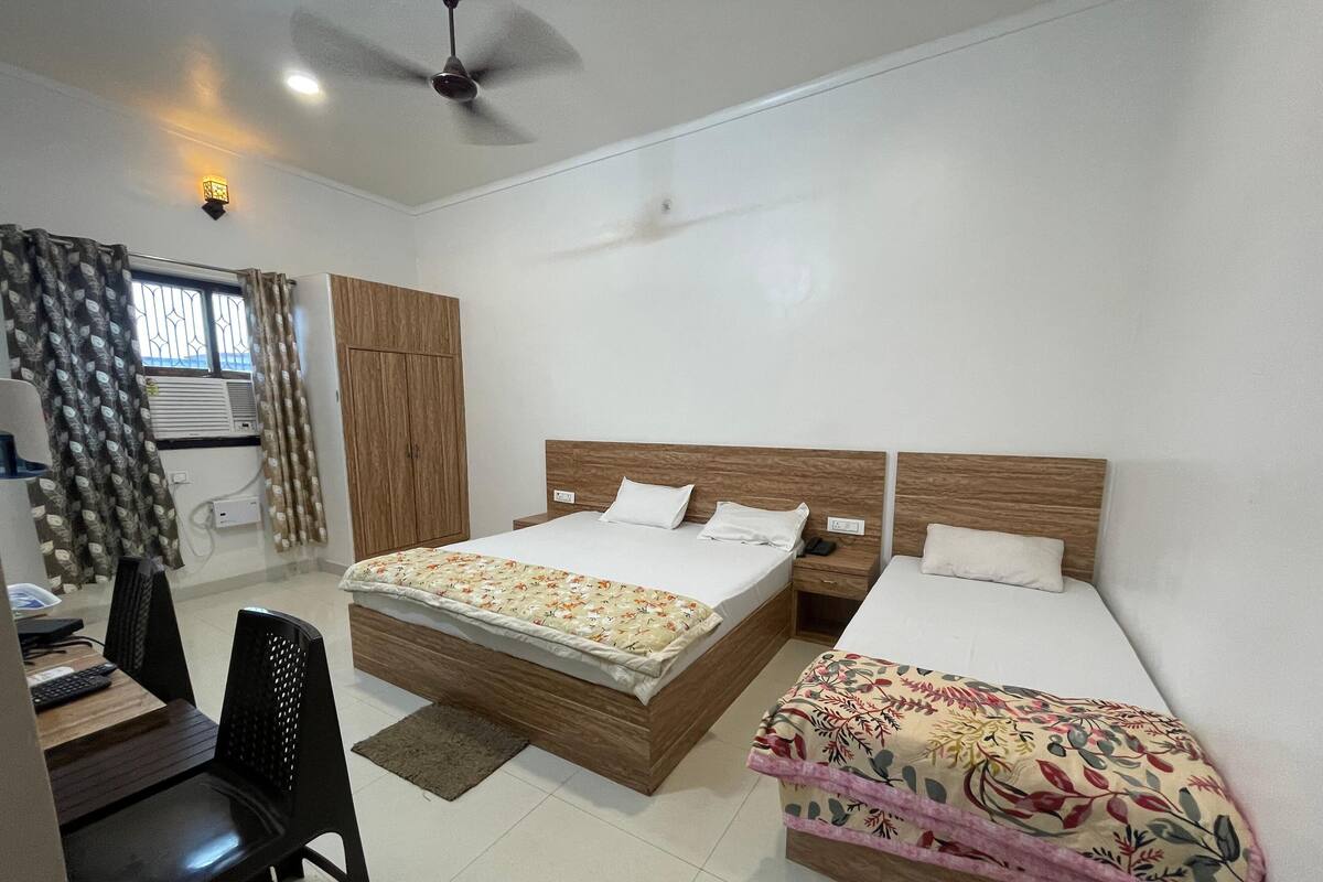 Une chambre avec deux lits, un bureau, une chaise, une armoire et un ventilateur de plafond.