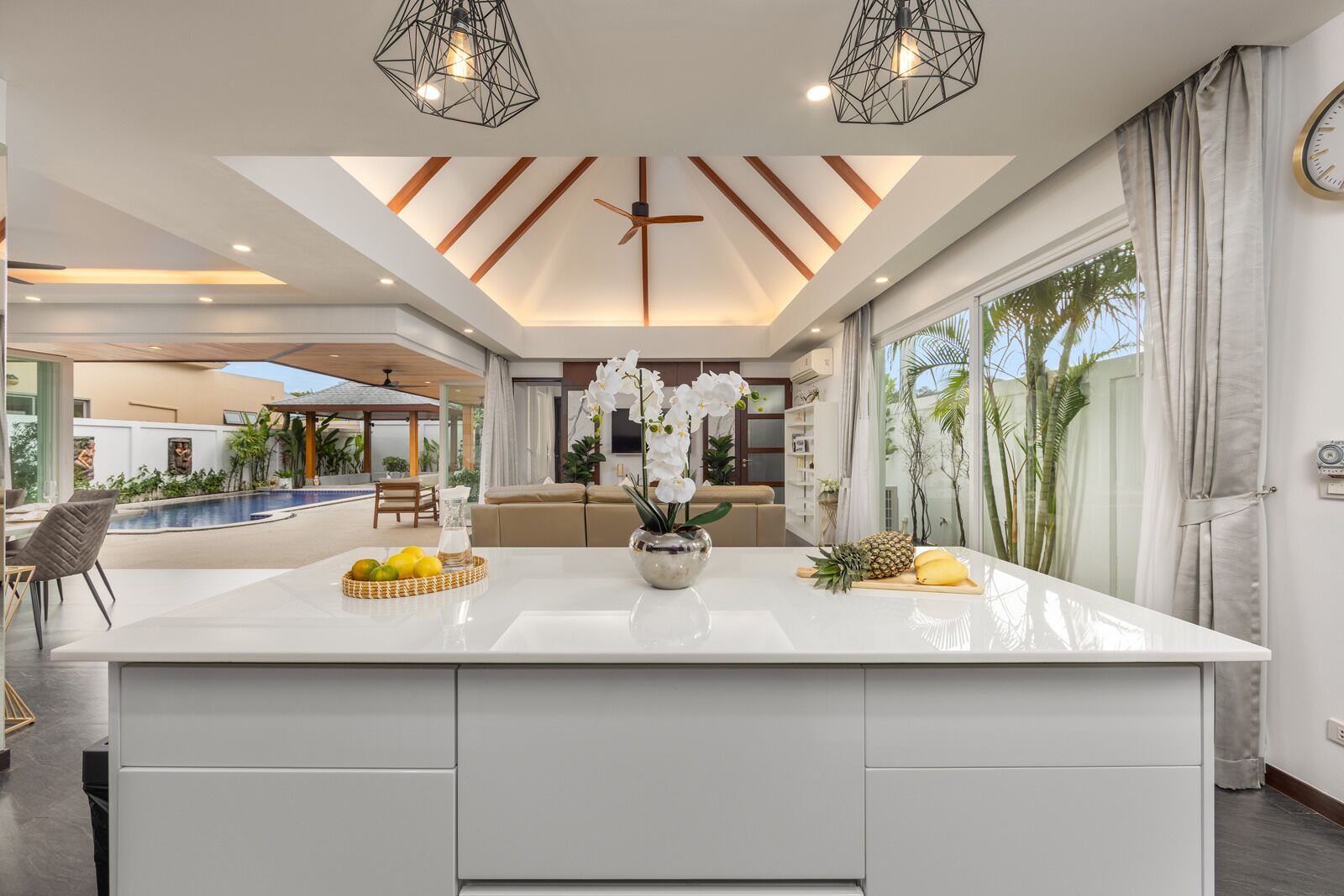 A modern kitchen with a central island, pendant lighting, and a view of the outdoor pool area.