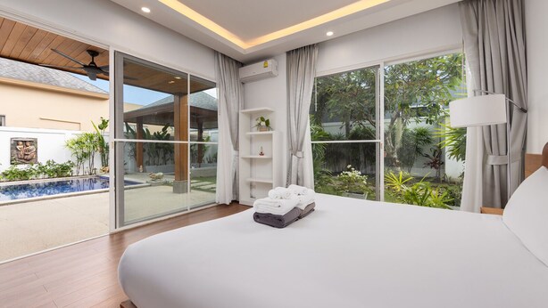 A modern hotel room with a large bed, a view of a swimming pool, and a balcony with plants. - Villa Hemi 2BR Modern Thai Style (Choeng Thale)