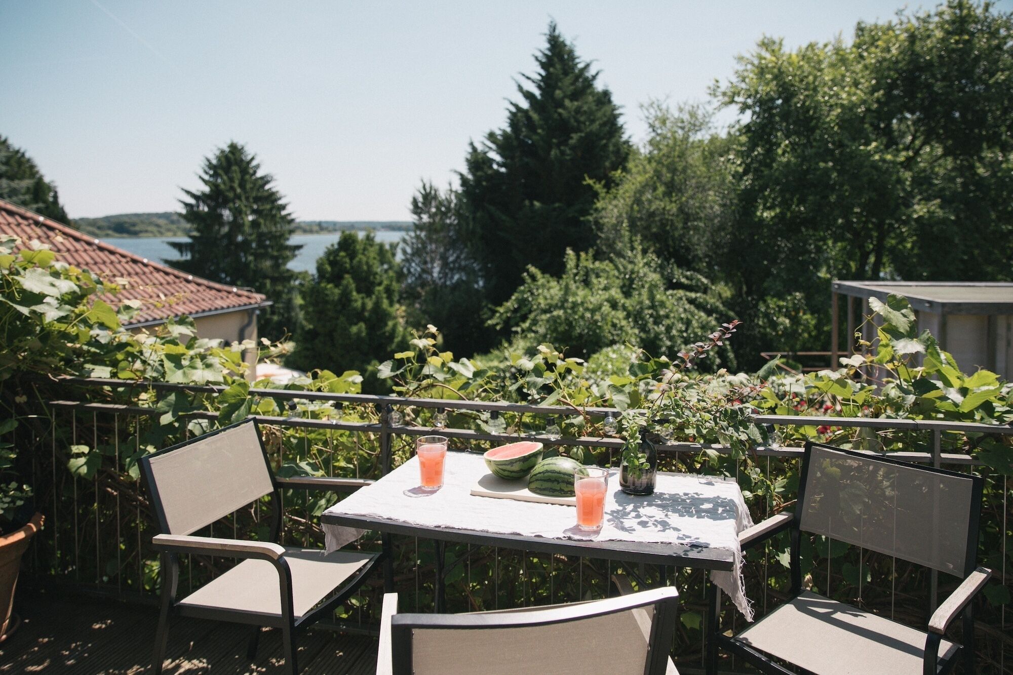 Un patio al aire libre con una mesa y sillas, con vista a un lago y rodeado de follaje.