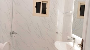 A bathroom with a marble wall, a sink, a mirror, and a shower. - Assistanceforfurnishedresidential units (Jeddah)