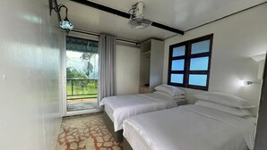 Een slaapkamer met twee bedden, een plafondventilator, een raam met zonwering en uitzicht op groen.