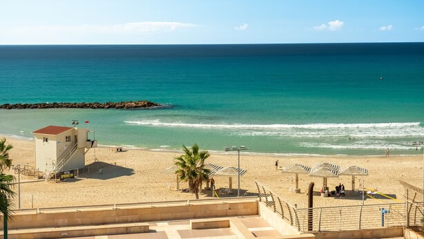 A beach with a lifeguard tower, umbrellas, and a clear view of the ocean. - Haifa Beachside Stay by Sea N' Rent (Haifa)