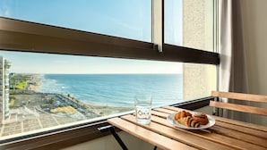 A table with a glass of water and pastries, overlooking a beach and ocean. - Haifa Beachside Stay by Sea N' Rent (Haifa)