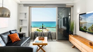 A modern living room with a black leather sofa, a wooden coffee table, and a large TV. A sliding glass door leads to a balcony with a view of the ocean. - Haifa Beachside Stay by Sea N' Rent (Haifa)