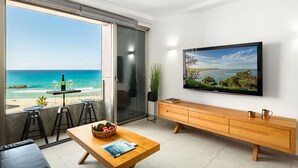 A modern living room with a large TV, a wooden dining table, and a view of the beach. - Haifa Beachside Stay by Sea N' Rent (Haifa)