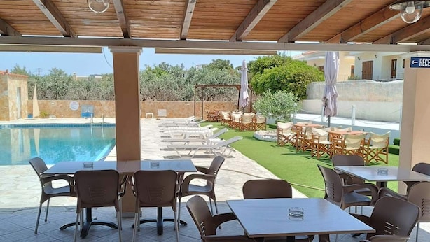 An outdoor patio with tables and chairs, a pool, and a view of the surrounding area. - GOLDEN BEACH (Aegina)