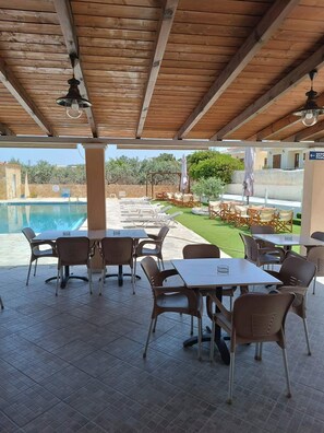 An outdoor patio with tables and chairs, a pool, and a view of the surrounding area. - GOLDEN BEACH (Aegina)