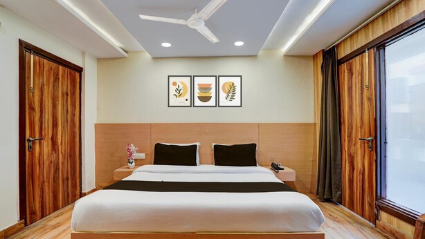 A hotel room with a large bed, wooden flooring, a ceiling fan, and framed artwork on the wall. - Super Collection O Dehradun Central (Dehradun)