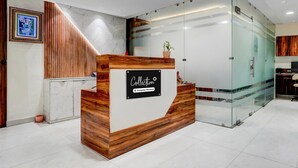 A reception desk with a wooden finish and a glass partition, a framed picture on the wall, and a potted plant on top. - Super Collection O Dehradun Central (Dehradun)