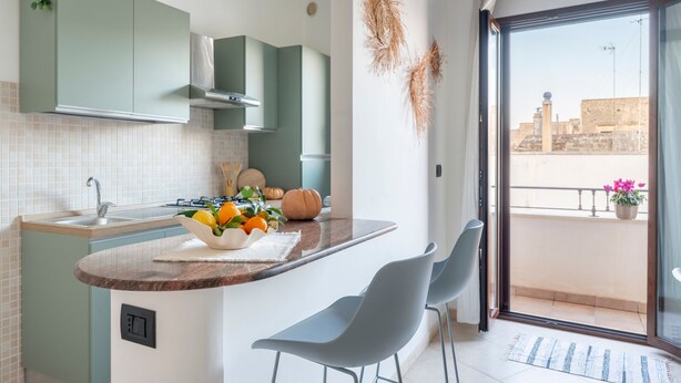Een moderne keuken met een centraal eiland, een eethoek met stoelen en een uitzicht op de stad vanuit een balkon.