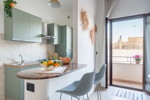 Eine moderne Küche mit Kochinsel, einem Essbereich mit Stühlen und Blick auf die Stadt vom Balkon.