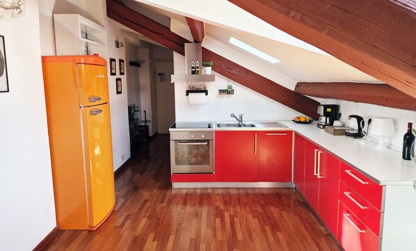 Une cuisine aux couleurs rouge et blanc, avec un plancher en bois, un four encastré et un évier moderne.