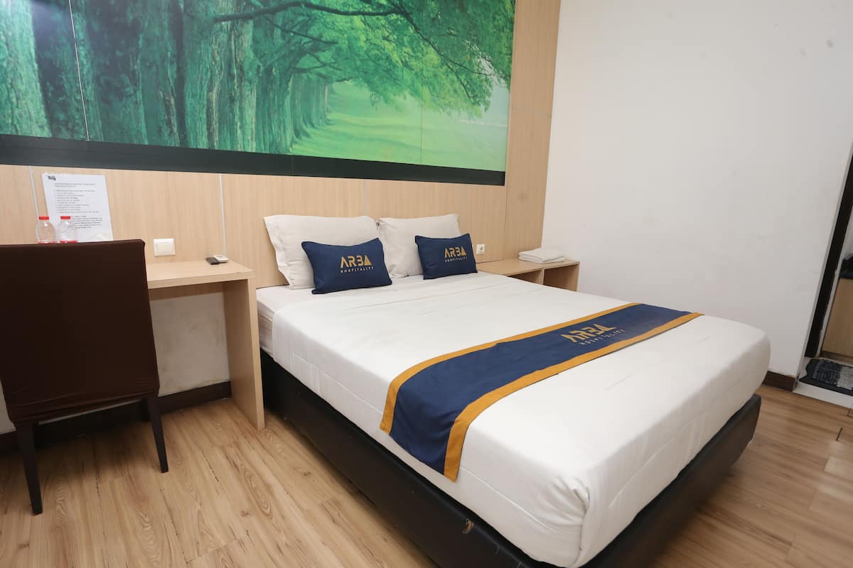 Habitación de hotel con cama, dos almohadas con el logotipo del hotel, mesita de noche con teléfono, una silla y un ventanal con vistas a árboles.