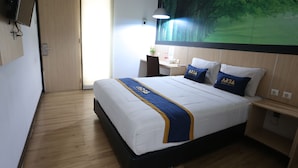 A hotel room with a bed, a desk, a chair, a TV, and a large window. - King Stone Hotel By ARBA (Bekasi)