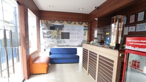A hotel lobby with a reception desk, a blue sofa, an orange bench, and a Coca-Cola refrigerator. - King Stone Hotel By ARBA (Bekasi)