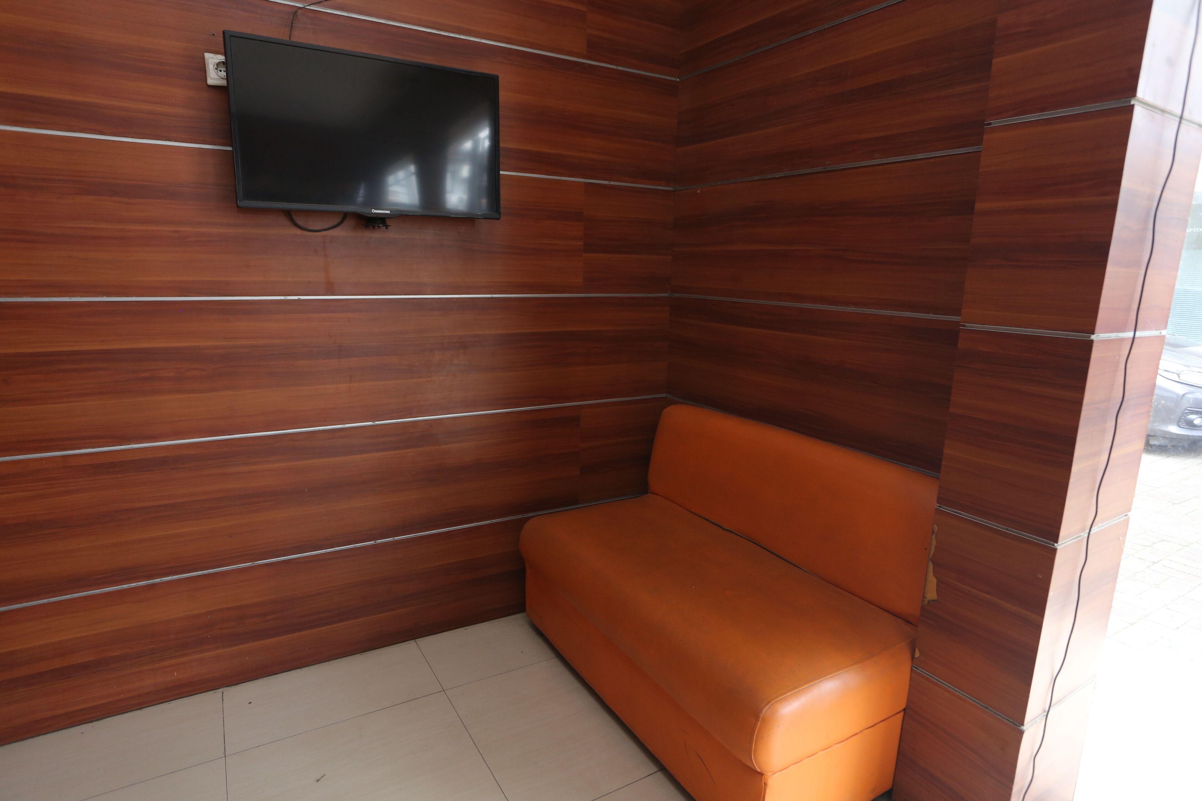 Quarto com parede de painel de madeira, televisão de tela plana acima de um sofá de couro marrom.