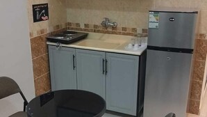 Une cuisine compacte avec des meubles gris, un évier, une cuisinière et un réfrigérateur. On y trouve deux chaises pliantes disposées autour d’une petite table ronde.