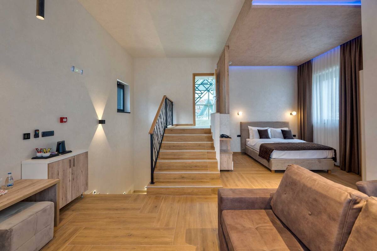 Una habitación de hotel moderna con una escalera de madera, una cama con cabecera, un sofá y un escritorio con una computadora.