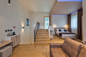 Una habitación de hotel moderna con una escalera de madera, una cama con cabecera, un sofá y un escritorio con una computadora.