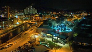 An aerial view of a cityscape at night with illuminated buildings, a river, and a parking area. - Aria City Boutique Hotel (Užice)