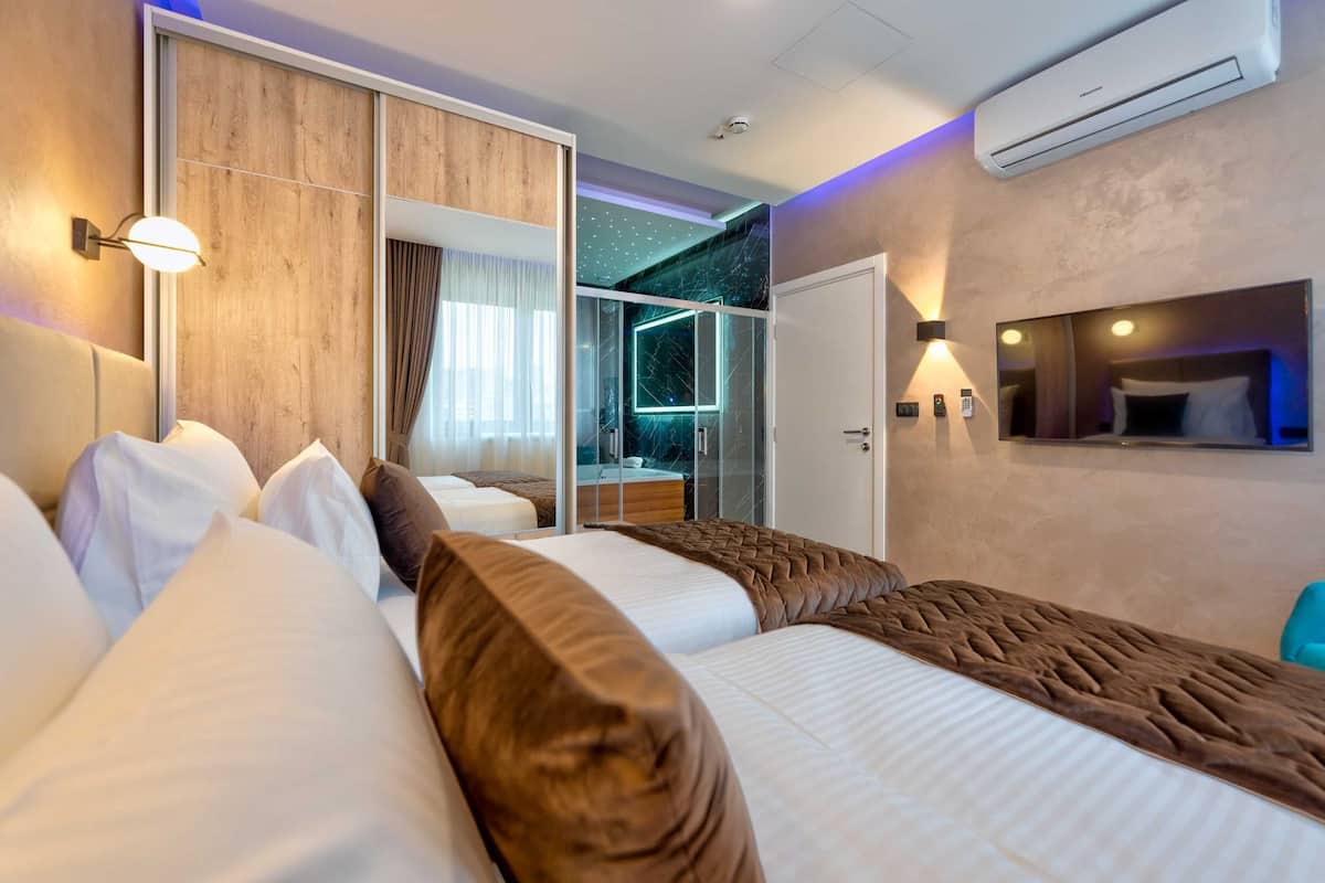 Habitación de hotel con dos camas, puerta corrediza a un balcón, un espejo grande y un equipo de aire acondicionado.
