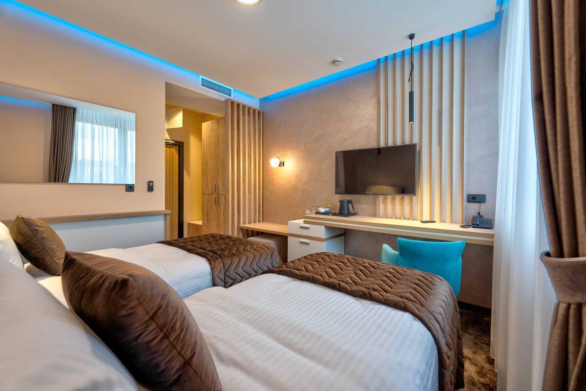 Habitación de hotel con dos camas, un escritorio, televisor y ventana con cortinas.