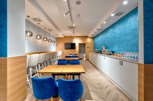 Un restaurante moderno con mesas de madera y sillas azules, un área de cocina y una pared decorada en azul.