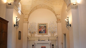 An interior with arched brick ceilings, a central altar with a painting, and pews arranged for seating.