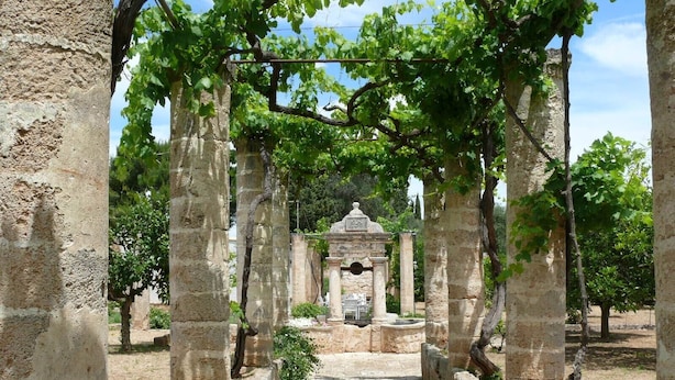 A stone pathway leading to a historical structure with arches and columns, surrounded by greenery.